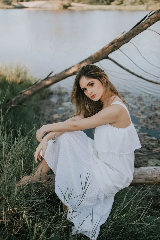Jovem de vestido branco sentada à beira do lago